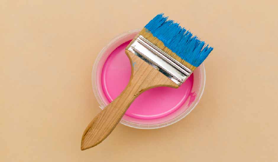 Görselde, pembe renkli saten boya kutusunun üstünde bir fırça var.