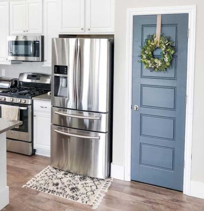 Görselde, mutfağa açılan mavi-gri renginde estetik bir ahşap kapı var.