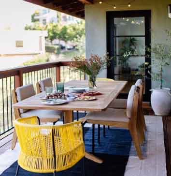 Görselde, beyaz duvarlı büyük bir balkon ve bu balkonun içerisinde yemek masası var.