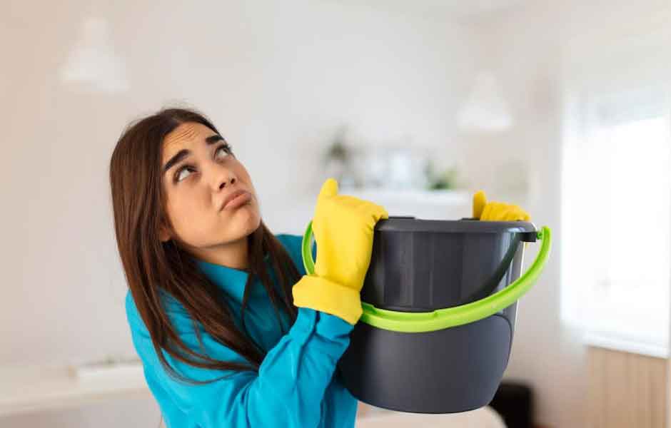 Görselde, kadın tavandan sızan su zemine akmaması için suyun altına kova tutuyor.