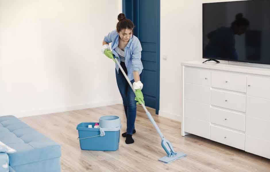 Görselde, genç bir kadın mikrofiber mop ile laminant parkeyi temizliyor.