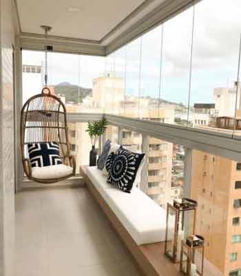 Cam Balkon Dekorasyonu Fikirleri. Görselde, içinde hamak sandalye, küçük sehpalar ve dar bir oturma bankı olan sade bir balkon var.