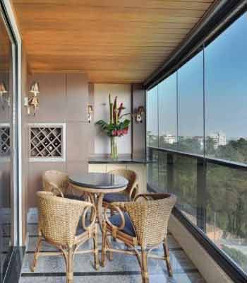 Cam Balkon Dekorasyonu Fikirleri. Görselde, içinde örgü masa ve sandalyeler olan ahşap tavanlı bir balkon var.