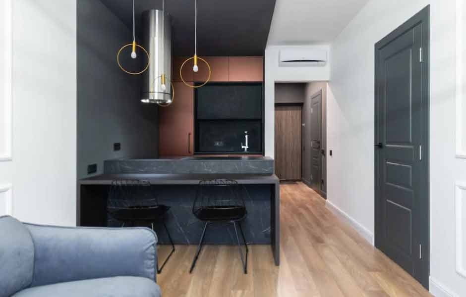 En iyi koridor boya renkleri konusu için kullanılan görselde, beyaz duvarları olan koridor, koyu gri renkli duvarlara sahip mutfağa doğru uzanıyor.