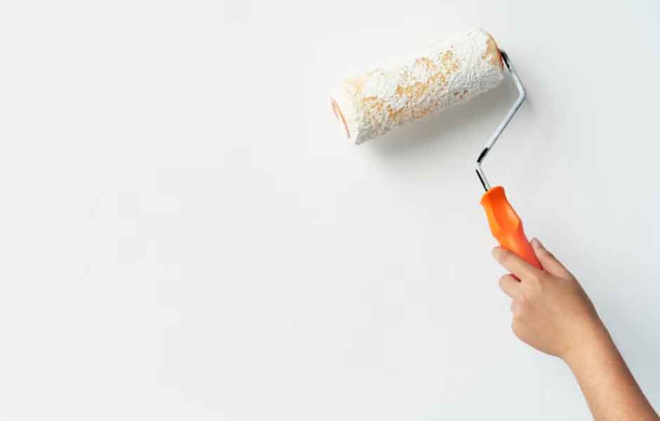 Ev nasıl boyanır sorusu için kullanılan görselde, ev sahibi, salonun duvarını boya rulosuyla beyaza boyuyor.