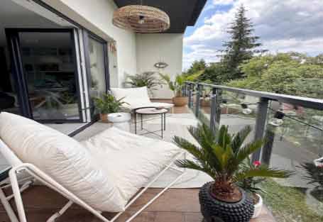 Görselde, beyaz duvarları ve beyaz koltukları olan huzurlu bir geniş balkon var.