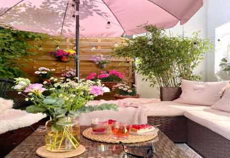 Geniş balkon dekorasyon fikirleri konusu için kullanılan görselde, içerisinde pembe şemsiye, koltuk takımı ve zeminde halı olan geniş bir balkon var.