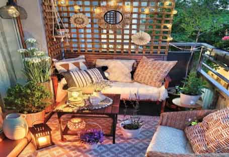 Görselde, ahşap duvarında dekor ürünleri ve içerisinde koltuk ve sehpa olan geniş bir balkon var.