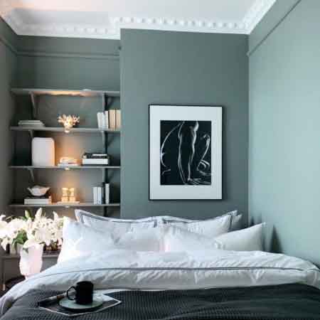 Küçük Oda Dekorasyonu Püf Noktaları. Küçük oda dekorasyonu için kullanılan görselde, mavi gri duvarlarında çerçeve ve rafların olduğu huzurlu bir yatak odası var.