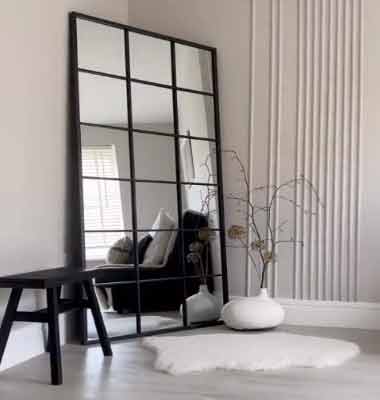 Küçük Odalar için Mobilya Seçimi – Büyük Ayna. Görselde, ahşap bir tabure ve küçük bir odayı daha geniş göstermeye yarayan duvara yaslanmış büyük bir ayna var.