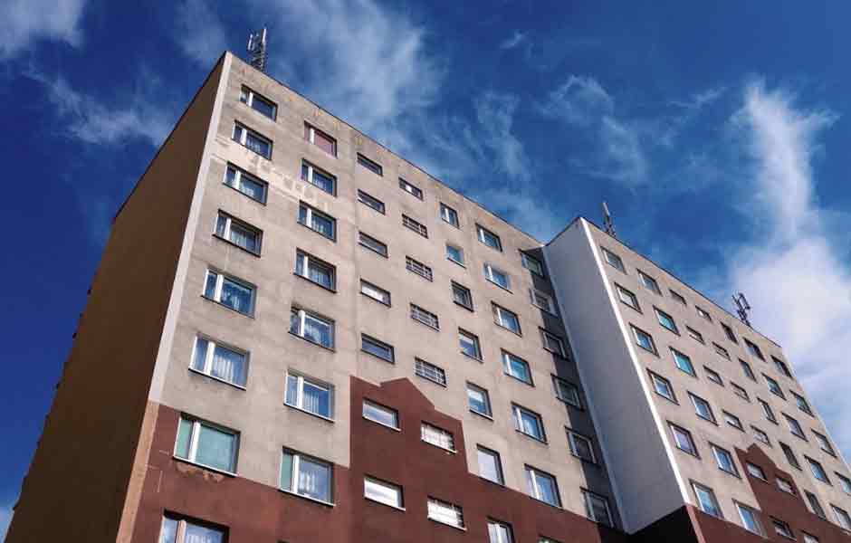 Görselde, dış cephesi kiremit ve beton rengi olması sebebiyle eski ve iç karartıcı duran yüksek katlı bir bina var.